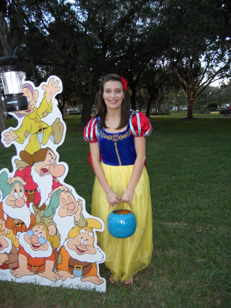 Young woman dressed as Snow White standing next to cardboard cutout of the seven dwarves